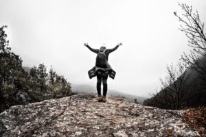 Person with arms raised on rocky mountain top, celebrating freedom and nature's beauty.