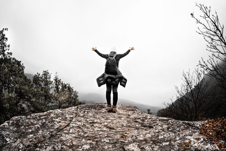 Person with arms raised on rocky mountain top, celebrating freedom and nature's beauty.